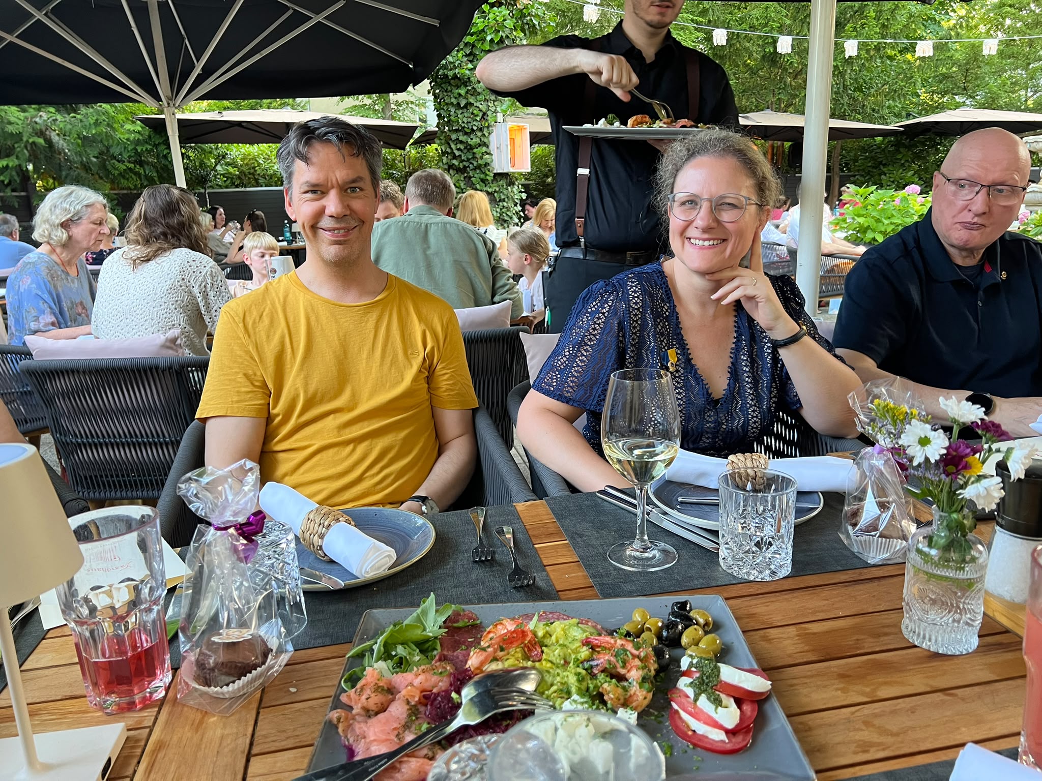 Drei Personen sitzen am Tisch und werden vom Kellner bedient