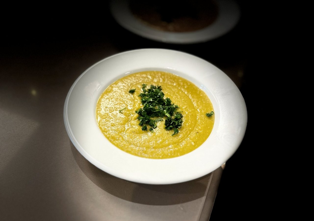 Ein tiefer Teller mit cremiger Erbsensuppe und einer Garnierung aus Kräutern in der Mitte.