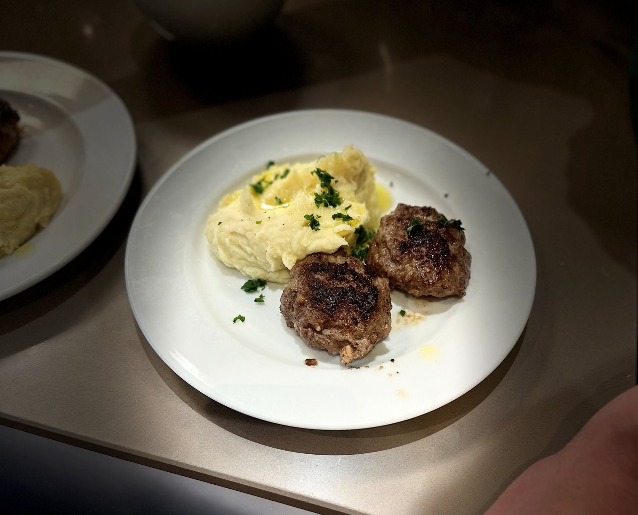 Ein Teller mit zwei gebratenen Buletten und Kartoffelstampf, garniert mit Kräutern.