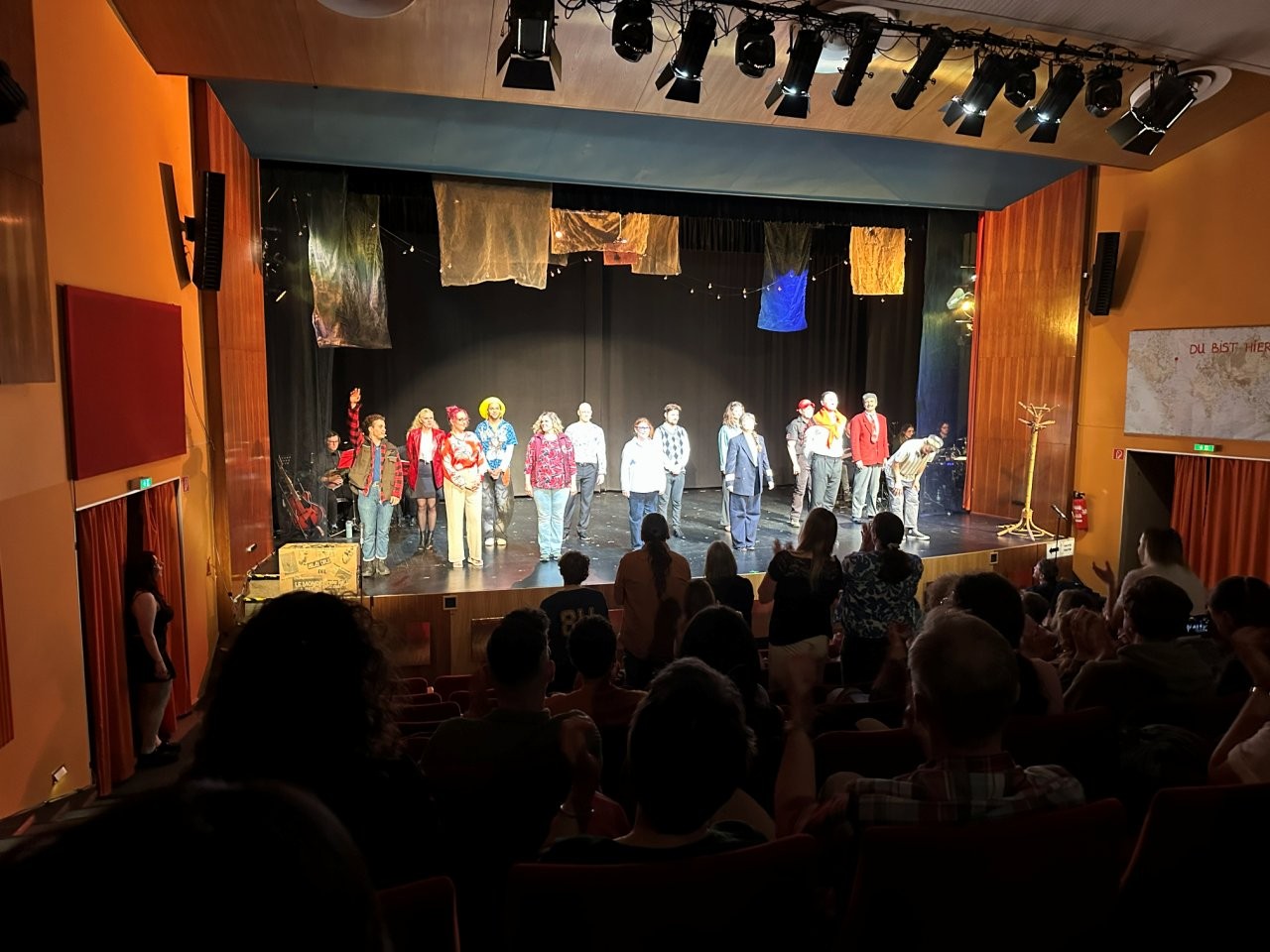 Ein Ensemble steht auf einer Theaterbühne, gesehen aus dem Zuschauerraum.