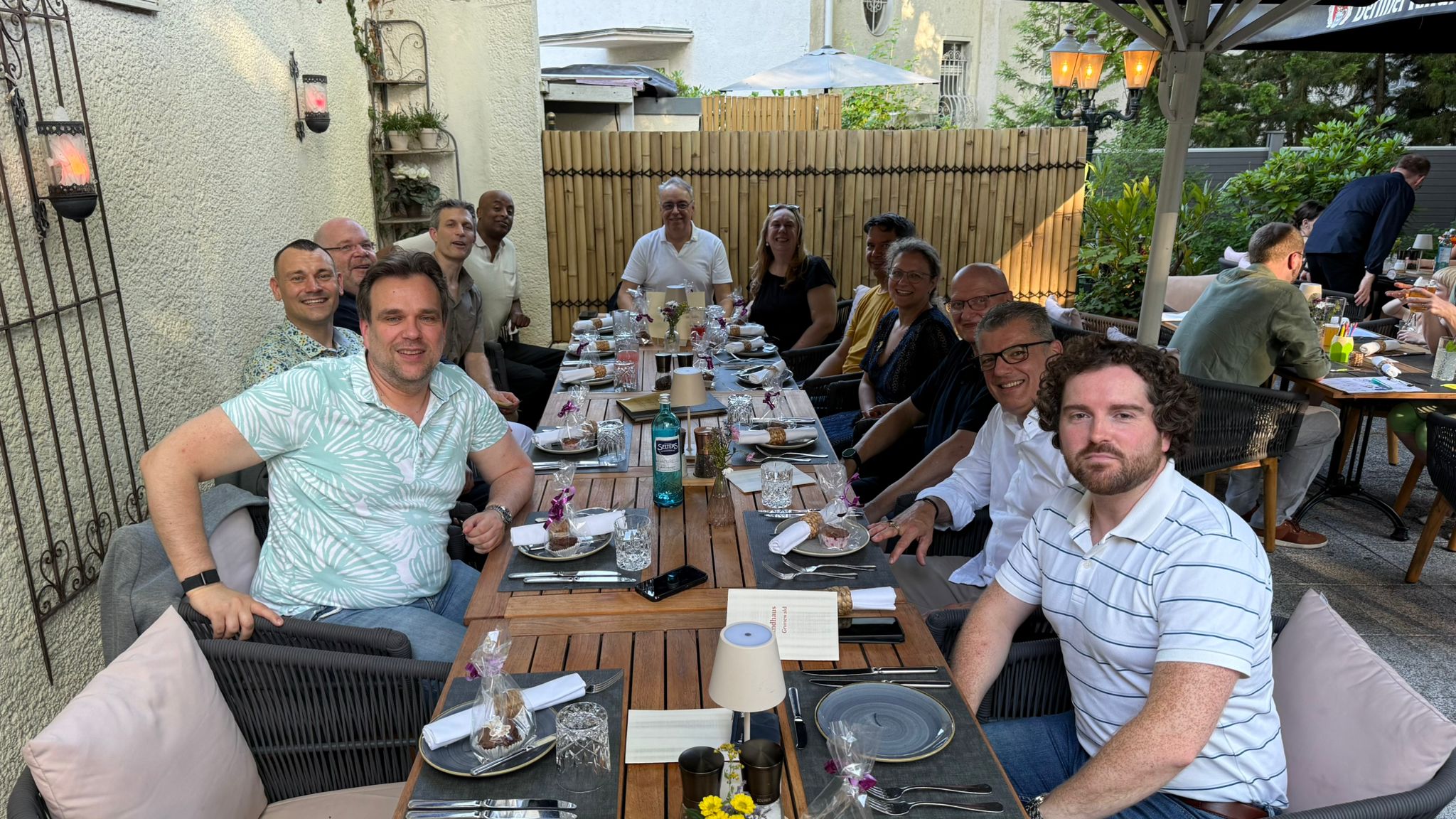 Mehrere Personen sitzen gemeinsam an einer festlich gedeckten langen Tafel in einem Außenbereich eines Restaurants.
