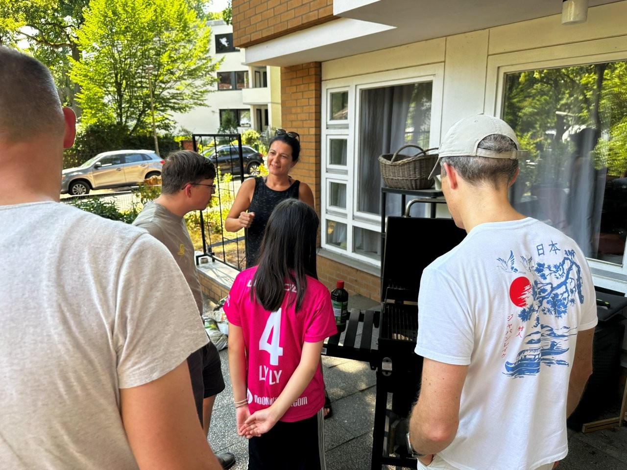Mehrere Personen stehen auf einer Terrasse um einen Grill herum
