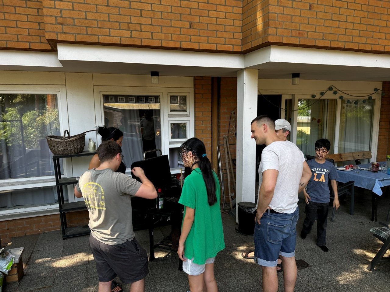 Mehrere Personen stehen auf einer Terrasse um einen Grill herum
